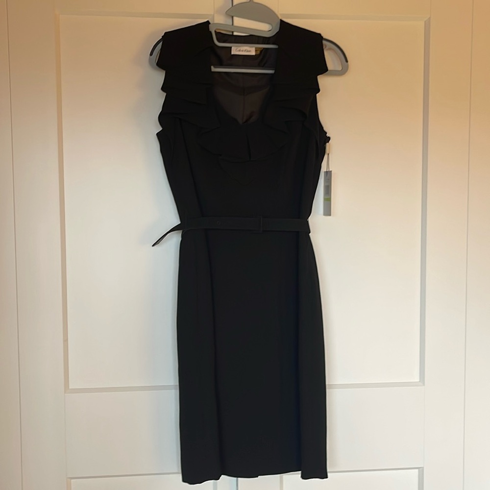 Calvin Klein black cocktail dress with ruffle at v neck, belt and side zipper.